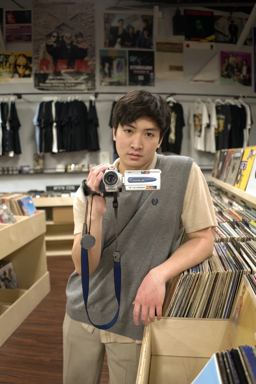 Portrait in a record store, holding up a silver camcorder