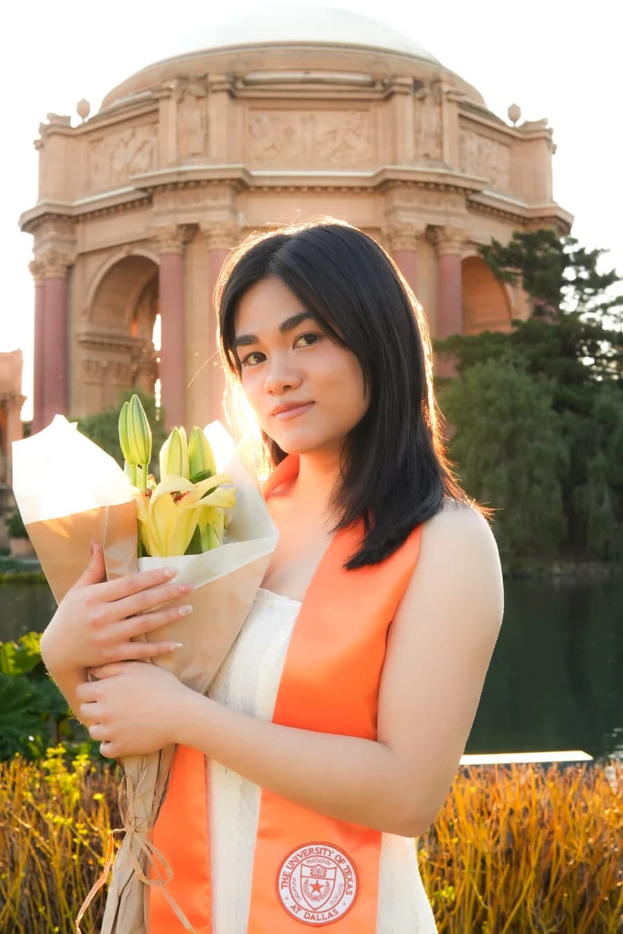 Graduate with lilies and an orange UT Dallas stole at the Palace of Fine Arts